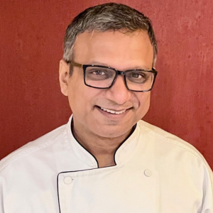 headshot of chef in chef jacket. Man with square rimmed glasses.